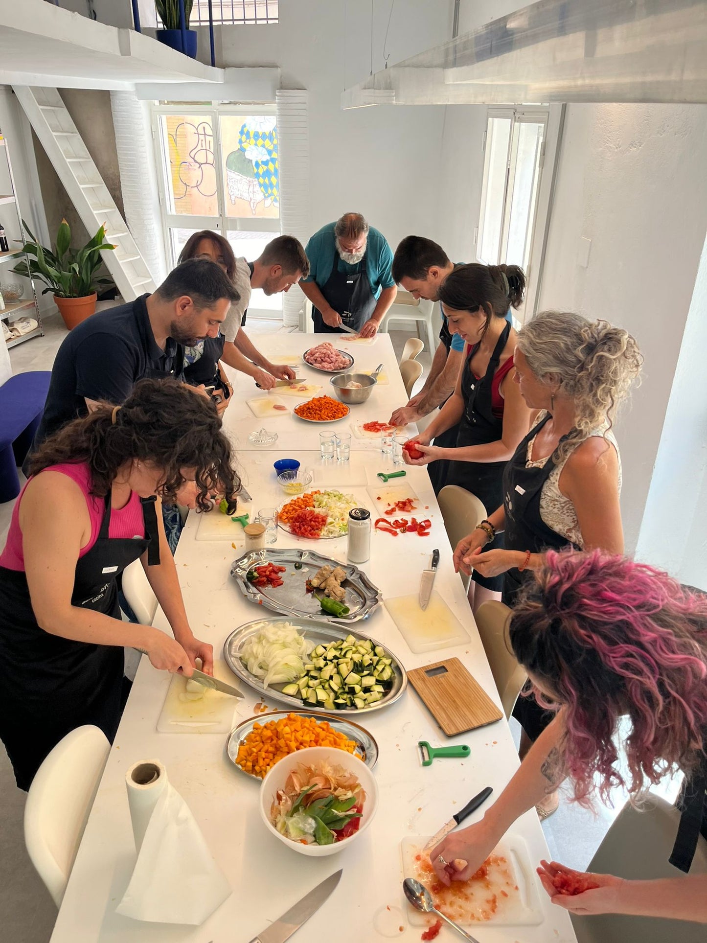 UNA GRUPO DE PERSONAS REUNIDOS AL REDEDOR DE UNA MESA, HACIENDO UN TALLER DE COCINA